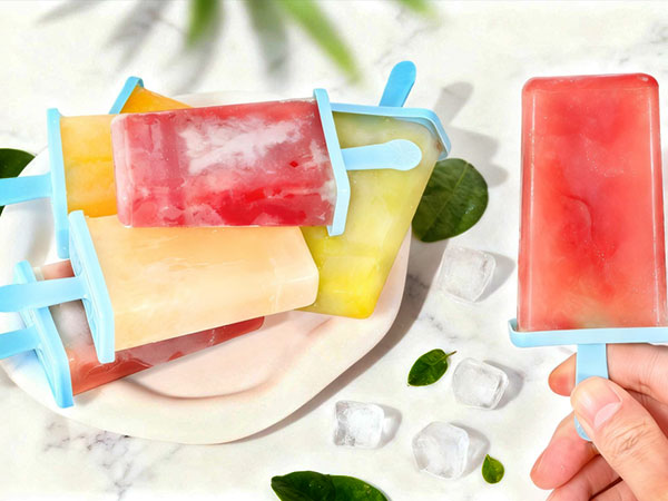 Watercolor illustration of colorful popsicles with bright red, orange, and yellow hues, scattered with green leaves on white background.
