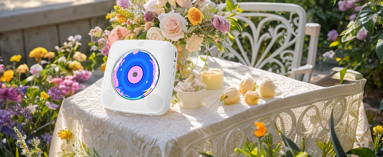 White ceramic speaker with blue and pink circular design on a garden table. Surrounded by flowers, candles, and refreshments in an outdoor setting.