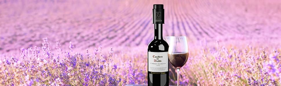 Wine bottle and glass on a small table in a lavender field. Purple flowers fill the background under a bright sky.