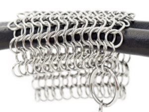 Stainless steel chainmail scrubber hanging on a grill handle.