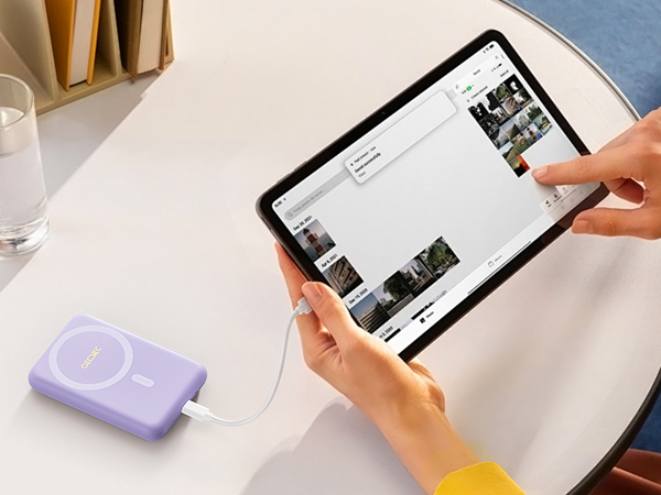a person holding a small ipod and charging it on a table.