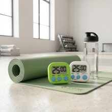 Compact digital timer on gym mat next to water bottle for interval workout tracking.