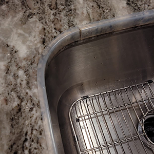 Close-up of a stainless steel sink drain with visible grate, surrounded by light-colored countertop or surface material.