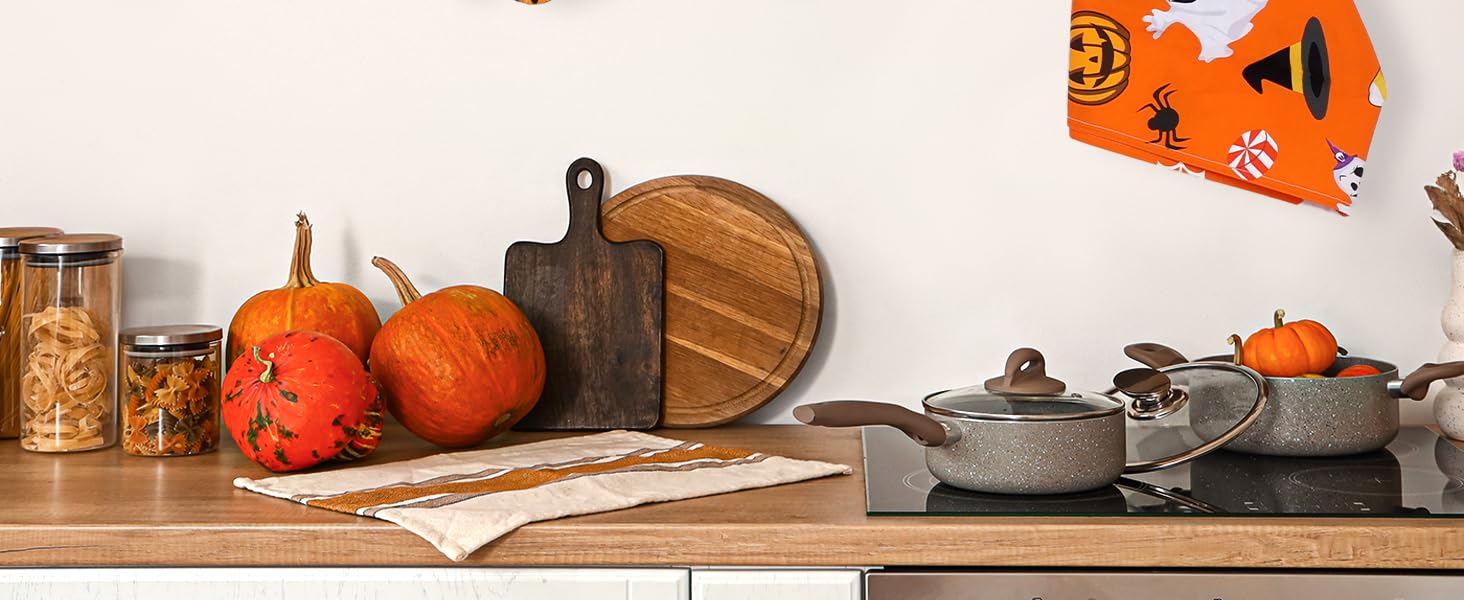 Halloween-themed kitchen accessories hanging on black rod, including oven mitts and pot holders in orange and black with pumpkin and ghost patterns.