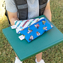Child holding a book with two zippered school supply packs on top, featuring Disney characters