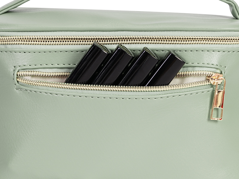 Close-up of a light green handbag or purse with a zippered compartment, showing black objects partially visible inside.