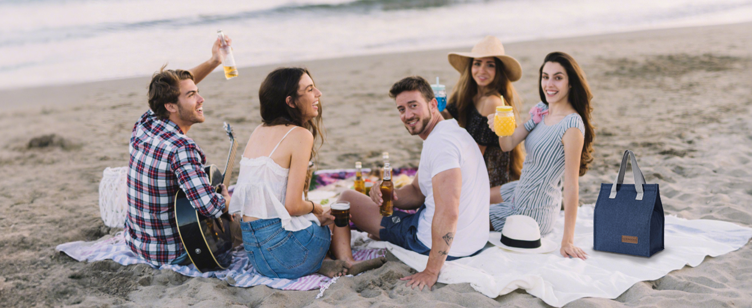 Group enjoying picnic on beach at sunset, with blanket spread out and cooler visible in scene.