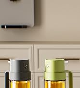 Two glass bottles with pump-top lids, one gray and one lime green. Bottles contain yellow liquid, possibly oil. Placed on counter beneath wall-mounted appliance.