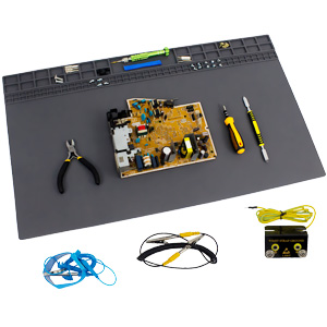 Electronic repair workspace with gray mat, circuit board, pliers, screwdriver, and various small components including wires and connectors.