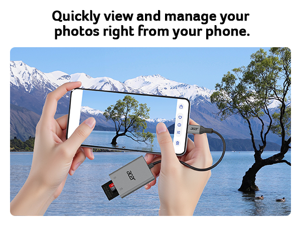 Hands holding smartphone capturing lake and mountain scene. USB drive attached, demonstrating photo management and viewing capabilities on mobile device.