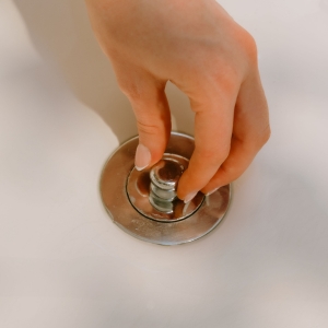 Hand replacing stopper on bathtub drain