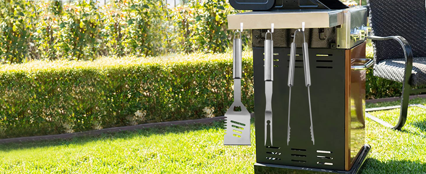 Outdoor grill cabinet with open doors, showing storage space and a hanging grill tool. Set in a garden with green hedges.