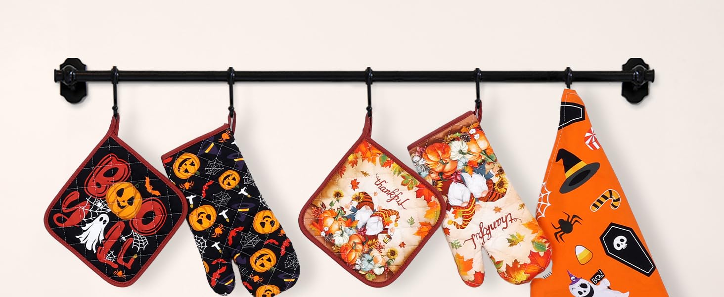 Halloween-themed kitchen accessories hanging on black rod, including oven mitts and pot holders in orange and black with pumpkin and ghost patterns.