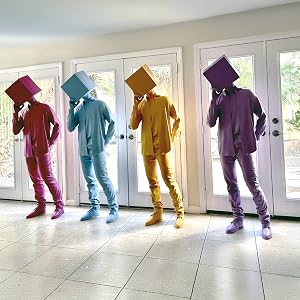 Four colorful human-like sculptures with cube heads posed indoors by glass doors