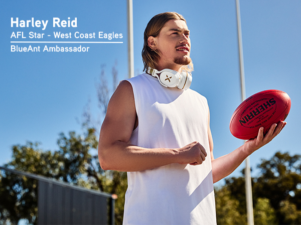 Harley Reid stands on an AFL field holding a football, wearing Pump X headphones around his neck