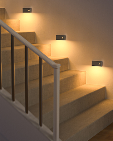 Motion-sensor LED stair lights mounted on walls, illuminating wooden steps with warm light. Metal handrail visible along the staircase.