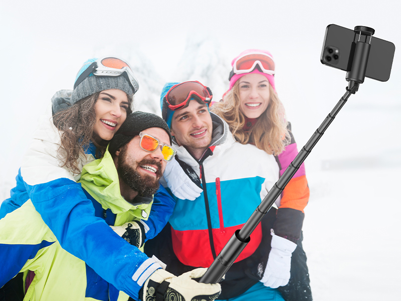 Extended selfie stick being used in snowy conditions, demonstrating outdoor photography capabilities in winter sport setting.