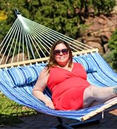 female model with sunglasses on blue striped quilted hammock with wooden spreader bars and pillow