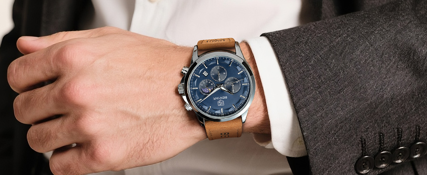 Men's wristwatch with blue dial, leather brown strap, and metal case worn on wrist with white shirt cuff visible. Classic analog watch styling with three subdials.