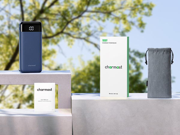 Outdoor scene with electronic devices on a white surface. Navy blue power bank, white boxes labeled 'charmast', and a gray drawstring pouch visible.