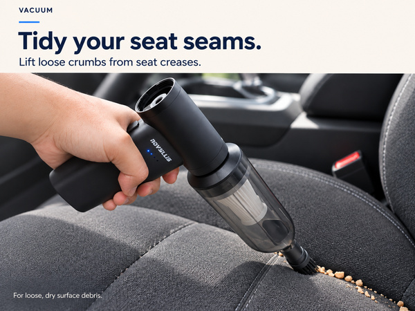 Cordless handheld vacuum collecting loose dry crumbs from fabric car seat seams