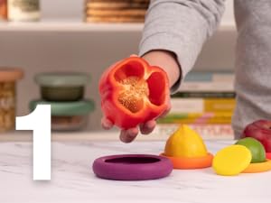 A red pepper is held over a silicone food saver with a lemon saver and lime saver on the counter