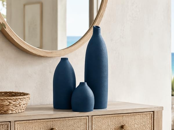 Matte navy blue vase set on an entryway console with woven accents, mirror, and ocean view.