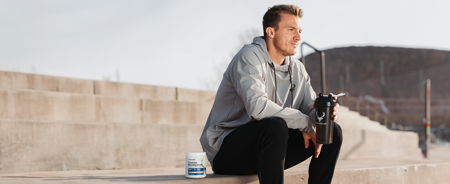 Man sitting on stairs outdoors holding Bucked Up Perfect Shaker bottle with Bucked Up Creatine
