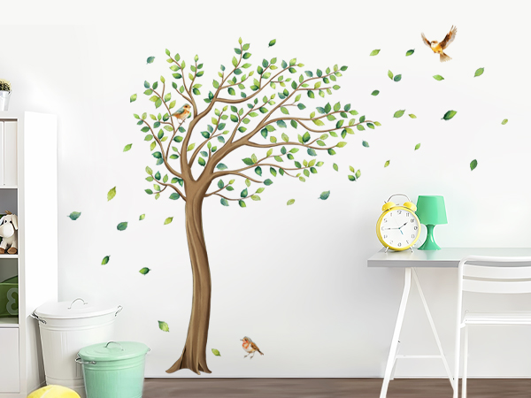 Wall decal featuring a green tree with spreading branches, floating leaves, and small birds, displayed on white wall near minimalist furniture.