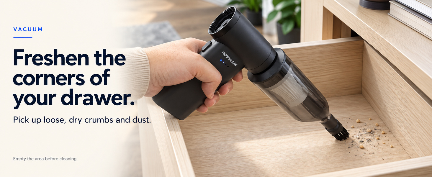Mini handheld vacuum collecting loose dry crumbs and dust from an empty wooden drawer