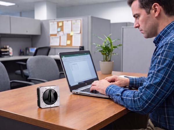 mechanical timer on an office desk next to a man using a laptop