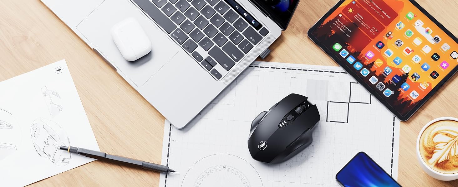 Desktop workspace setup showing a wireless mouse, laptop, mobile device, and writing materials arranged on a wooden surface.