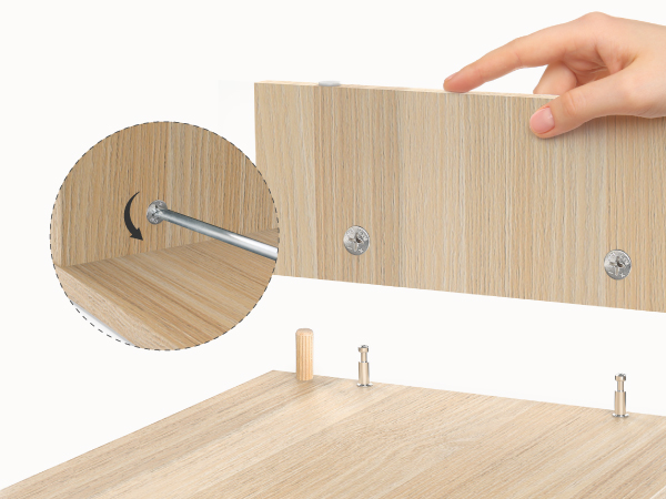 Close-up of wooden furniture assembly, showing screwdriver inserting hardware into pre-drilled holes in light-colored wood panel.