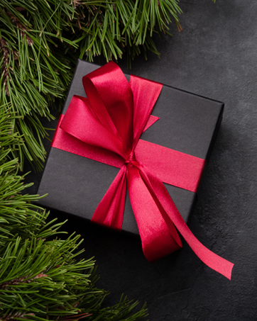 Gift box with red ribbon on a stone table top with green garland