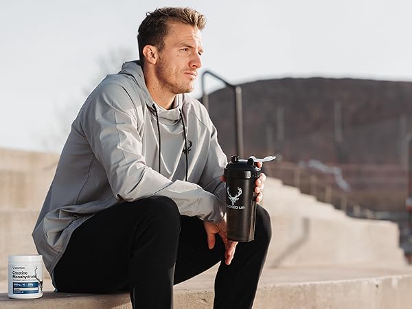 Man sitting on stairs outdoors holding Bucked Up Perfect Shaker bottle with Bucked Up Creatine