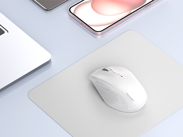 White wireless computer mouse on a light gray mousepad, next to a laptop and smartphone on a white surface.