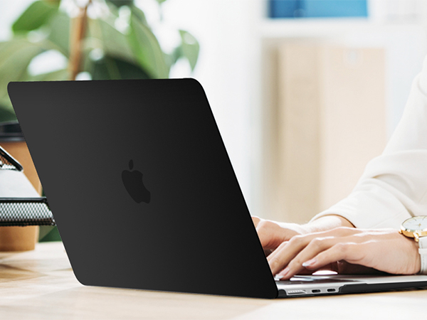 Matte black laptop computer in use on light wooden desk with green plant visible in background.