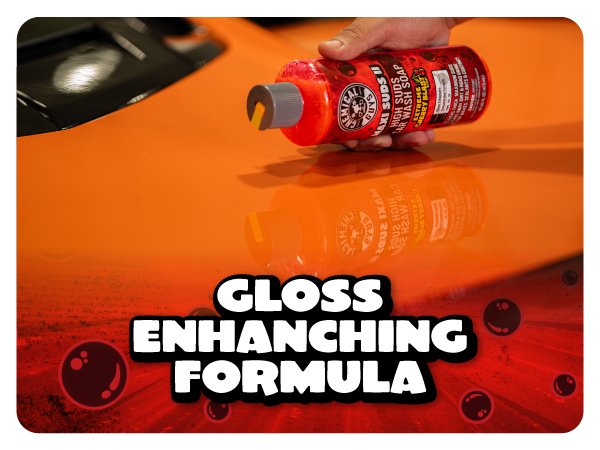 Detailer wipes thick foam across a black sedan hood with a green wash mitt during a two-bucket wash