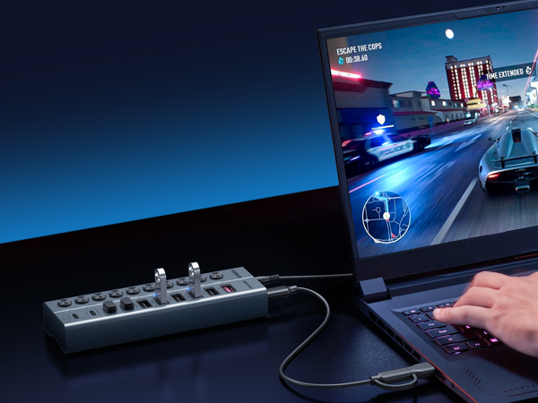 Gaming setup showing computer monitor displaying racing game with blue vehicle headlights, keyboard with illuminated keys, and hand on mouse during active gameplay session.