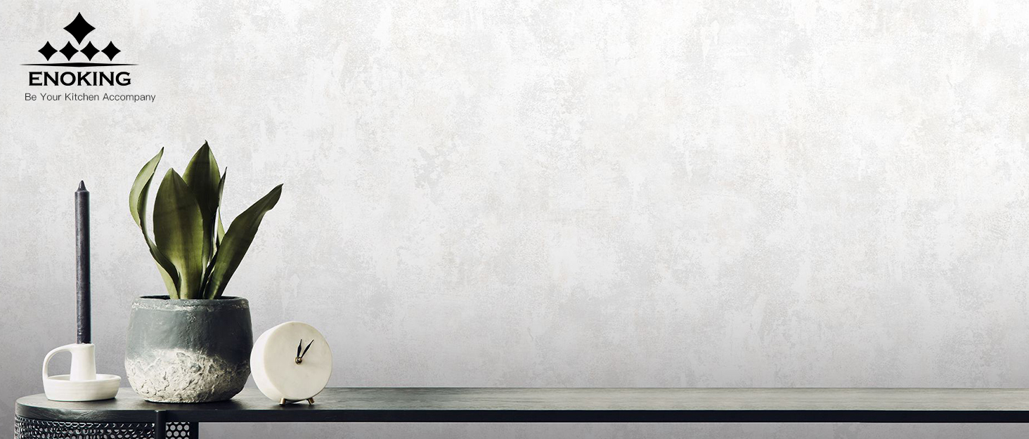 Minimalist home decor scene with potted plant, candle, and decorative objects on a surface against a white textured wall.