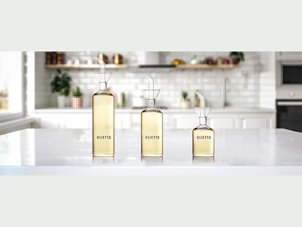 Three glass bottles with amber-colored liquid displayed on white marble countertop in modern kitchen setting.