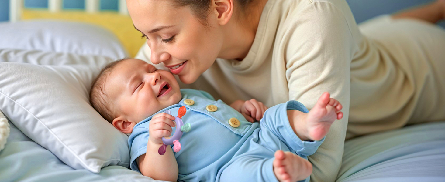 A newborn baby wearing a light blue onesie with colorful buttons lies on a white pillow. The baby's arms are outstretched and eyes are closed.