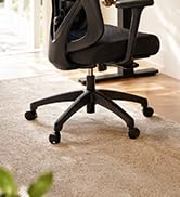 Black office chair with wheels and adjustable back support positioned on light wooden floor with green plant visible at base.
