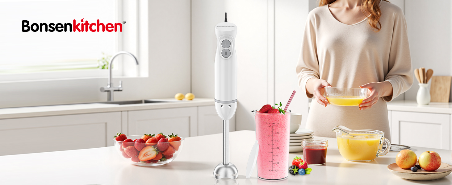 Handheld immersion blender being used in kitchen. Person blending fruits in glass. Countertop with fruits and blender accessories visible.