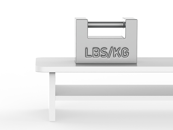 Small, rectangular metal weight marked 'LBS/KG' resting on a white surface. Features a handle cutout.