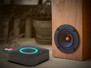 Modern audio setup showing a black circular speaker with blue LED ring light alongside a wooden bookshelf speaker with visible driver cone.