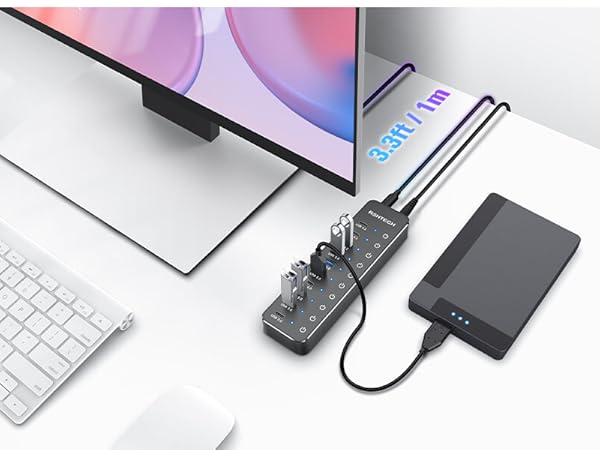 Desktop setup with curved monitor, wireless keyboard, USB hub, external hard drive, and smartphone on white surface. Gold-framed handbag visible in corner.