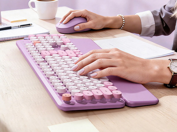 Typing on a lavender purple retro wireless keyboard with matching mouse on a bright office desk.