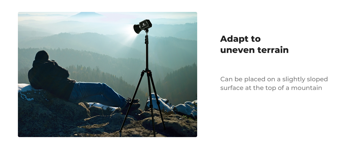Camera tripod on rocky mountain terrain, demonstrating adaptability to uneven surfaces. Misty mountain landscape in background. Text describes placement on sloped surfaces.