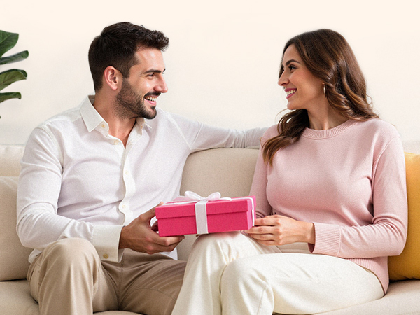 Multiple images showing people sitting on a couch, interacting casually in a home setting. One person holds a small gift box with pink wrapping.